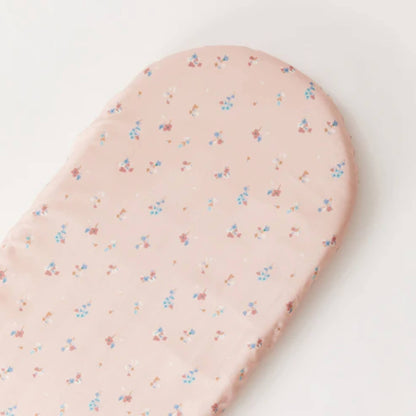 An oval baby mattress fitted with a pale pink floral cotton sheet, photographed against a light background to show shape and fit.