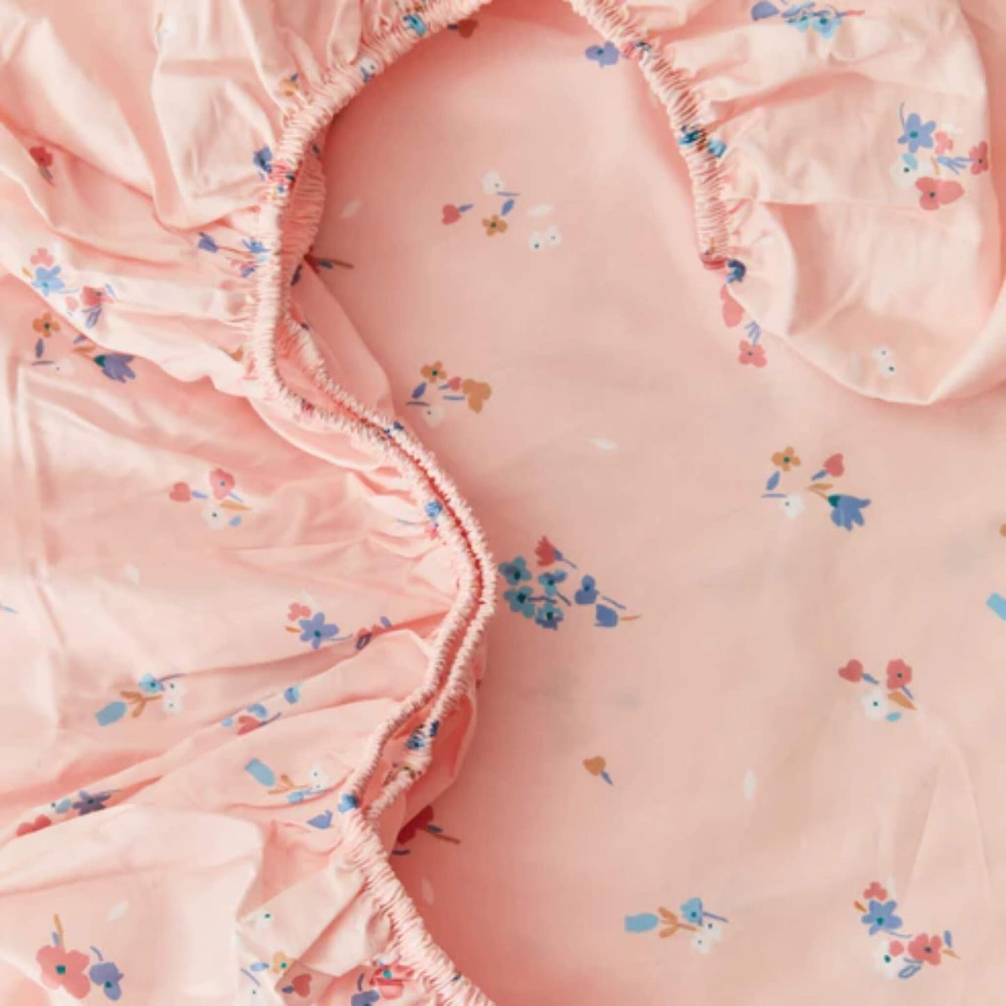 A close-up of elasticated sheet edges in pink cotton fabric, showing gathered stitching designed to keep the sheet securely in place.
