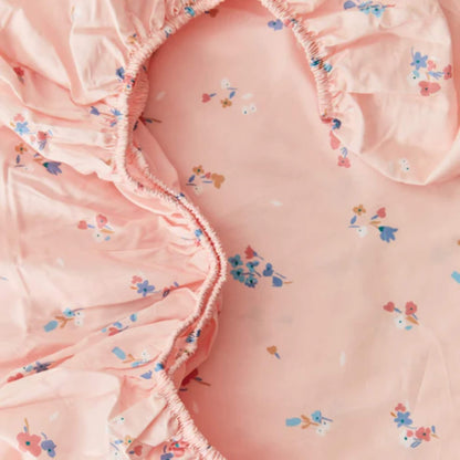 A close-up of elasticated sheet edges in pink cotton fabric, showing gathered stitching designed to keep the sheet securely in place.