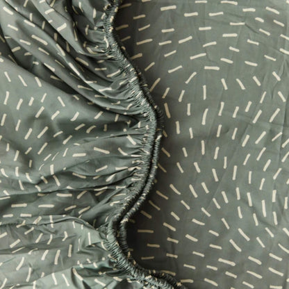 Close-up of organic cotton fitted sheet fabric in sage green with white dash pattern, showing smooth texture.