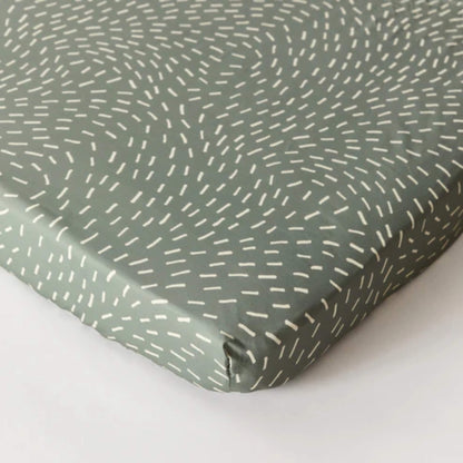 Kabode organic cotton fitted sheet in Dashes print, shown fitted over a mattress corner in soft sage green with white dash pattern.
