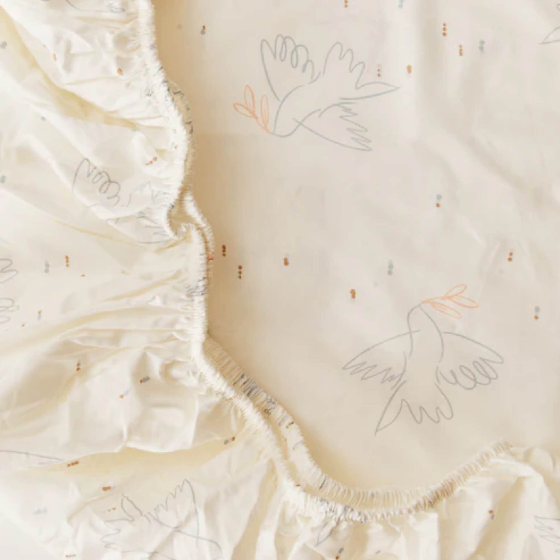A detailed close-up of elasticated edging on a fitted sheet, showing gathered stitching and printed bird motifs on cream fabric.