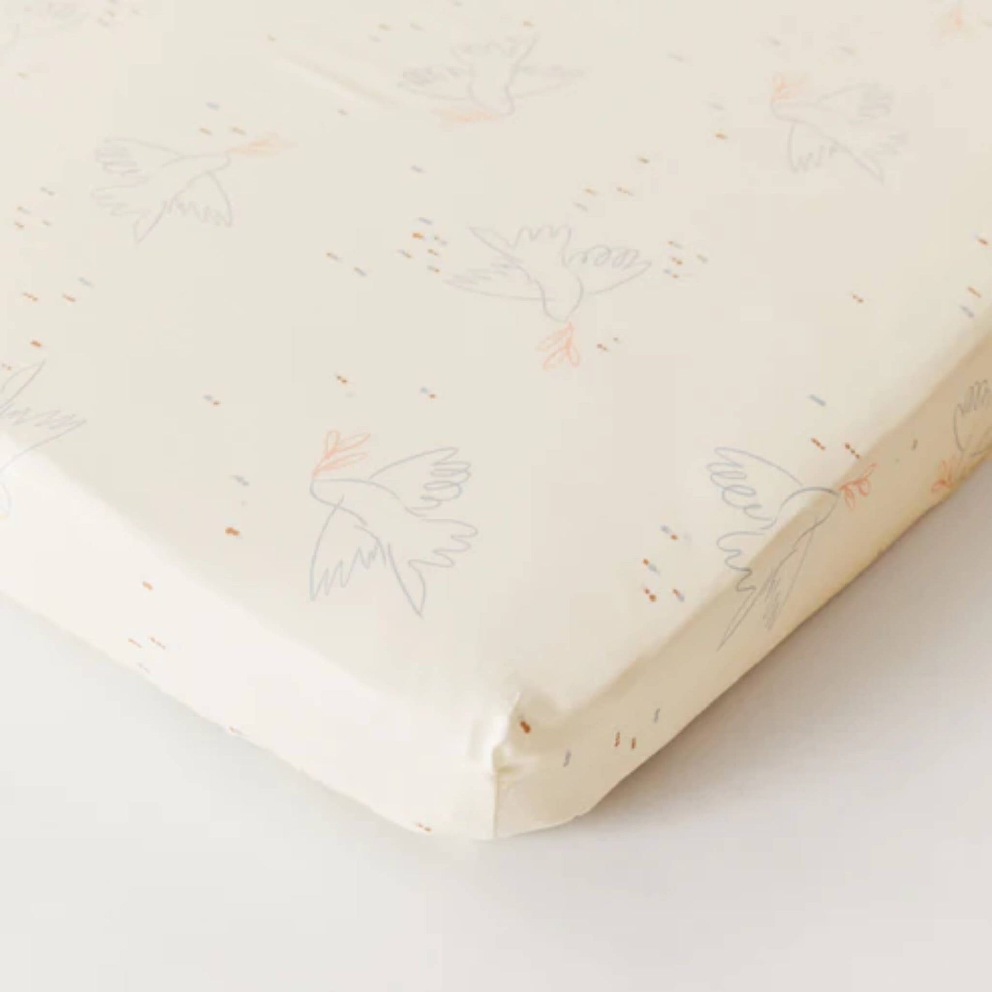Kabode Dove organic cotton fitted sheet shown neatly fitted over a mattress, with a soft cream base and delicate bird illustration pattern.