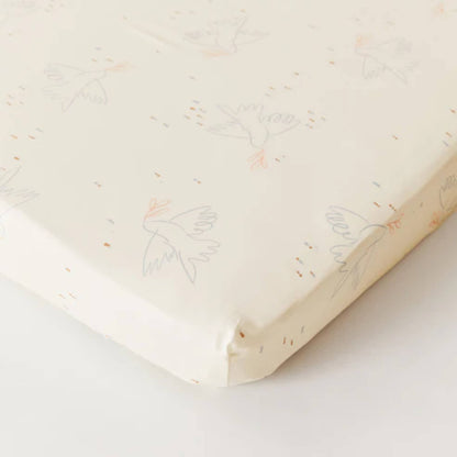 Kabode Dove organic cotton fitted sheet shown neatly fitted over a mattress, with a soft cream base and delicate bird illustration pattern.