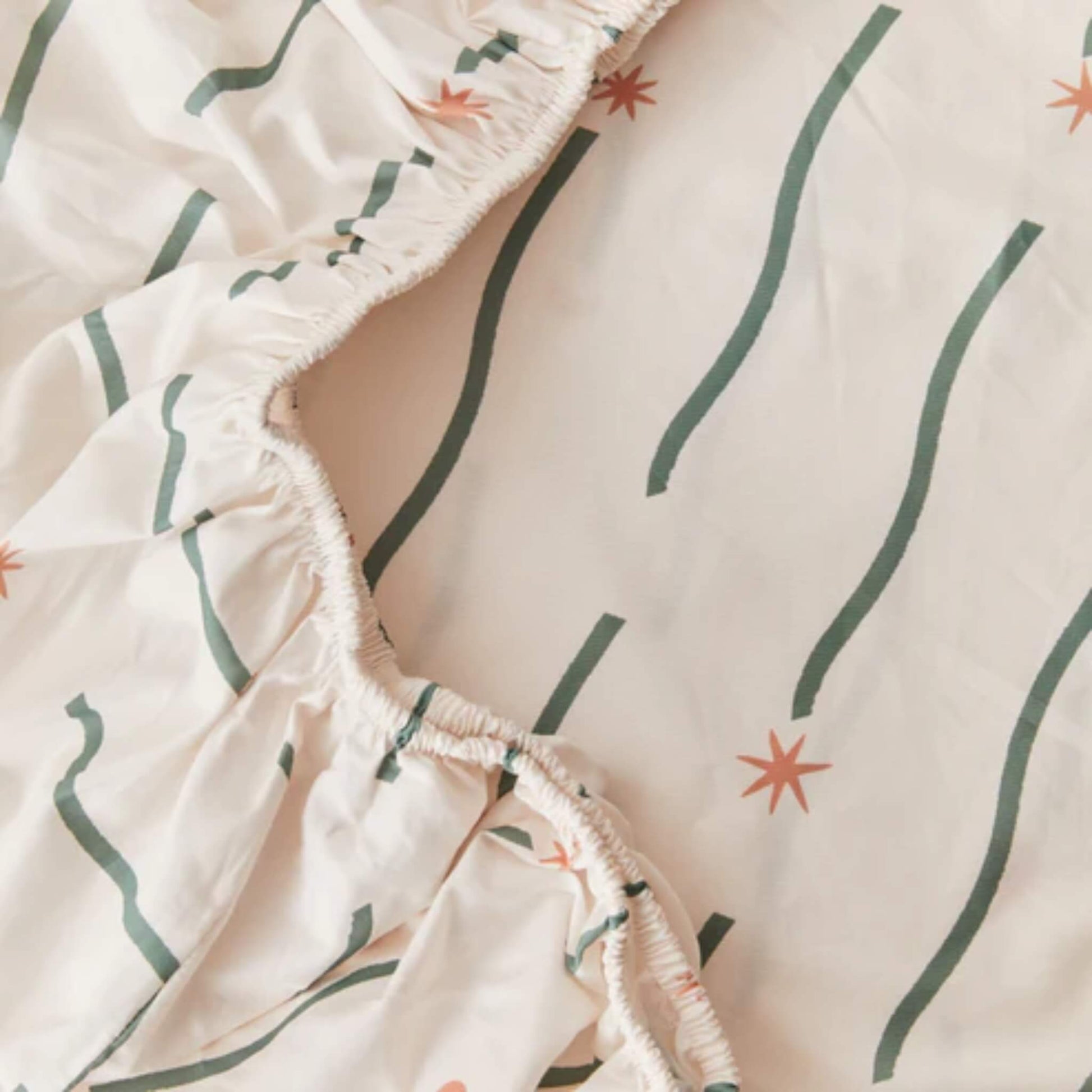 Detail view of elasticated edging on a fitted sheet, highlighting gathered stitching and soft organic cotton fabric.