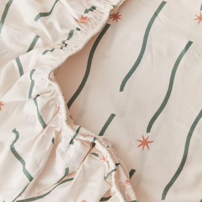 Detail view of elasticated edging on a fitted sheet, highlighting gathered stitching and soft organic cotton fabric.