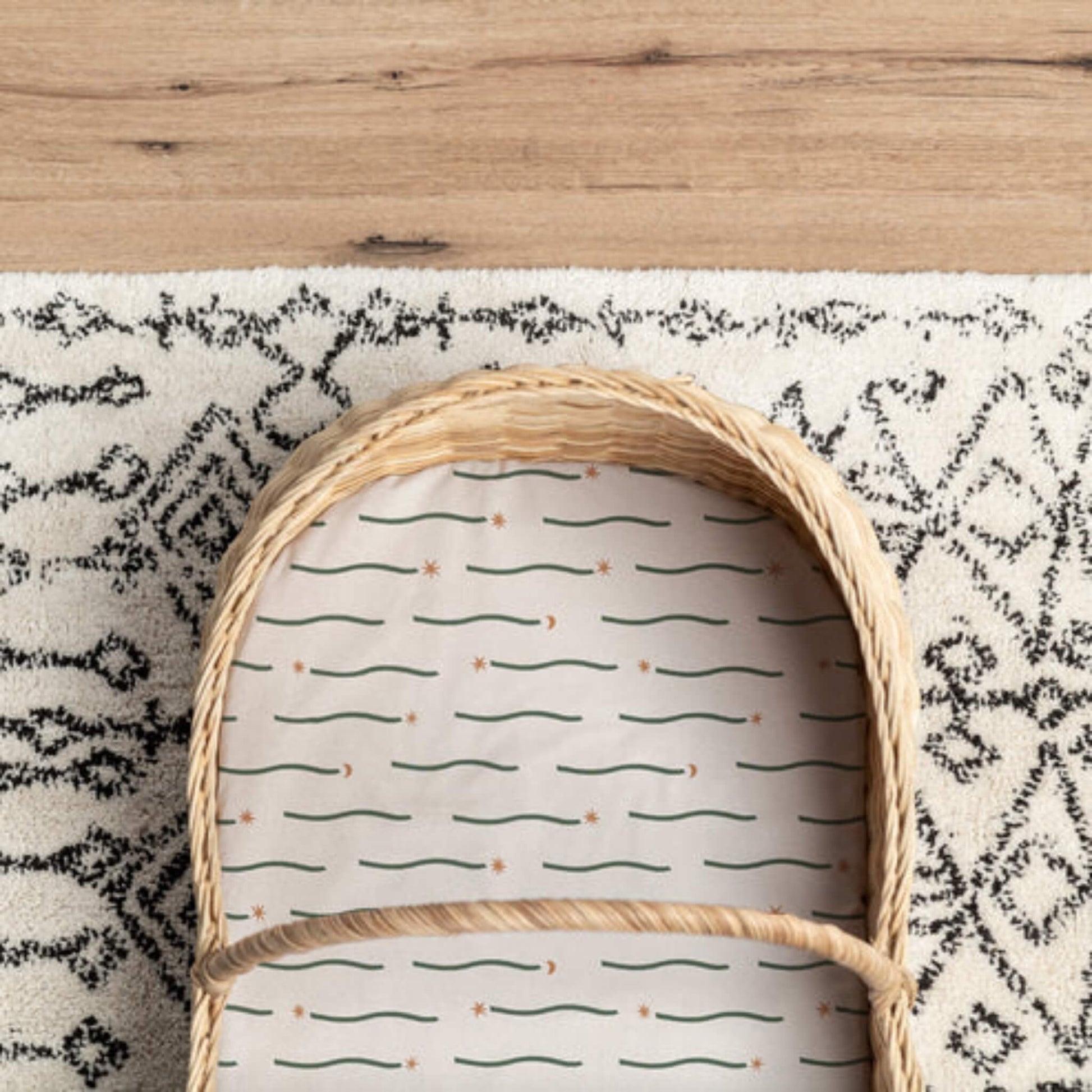 Moses basket mattress covered with a fitted sheet in a Night Sky print, showing pattern scale and fit within a woven basket.