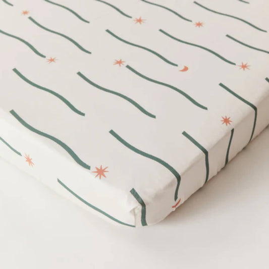 Kabode Fitted Sheet in Night Sky design laid over a mattress, showing a soft organic cotton surface with green wavy lines and small star motifs.