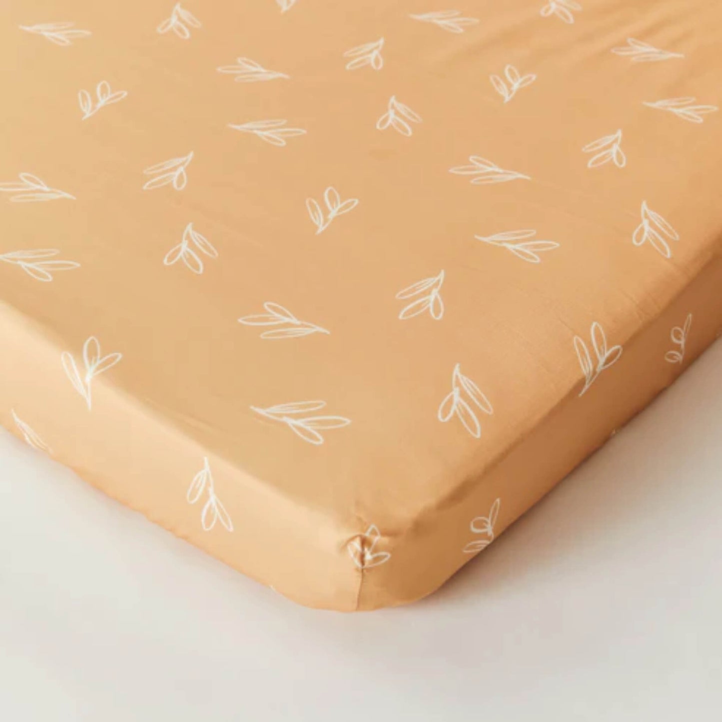 Kabode organic cotton fitted sheet in Olive Sprig print, shown neatly fitted over a mattress with elasticated corners and a warm mustard tone.
