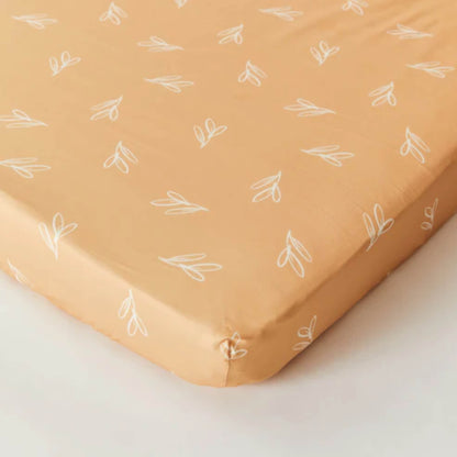 Kabode organic cotton fitted sheet in Olive Sprig print, shown neatly fitted over a mattress with elasticated corners and a warm mustard tone.