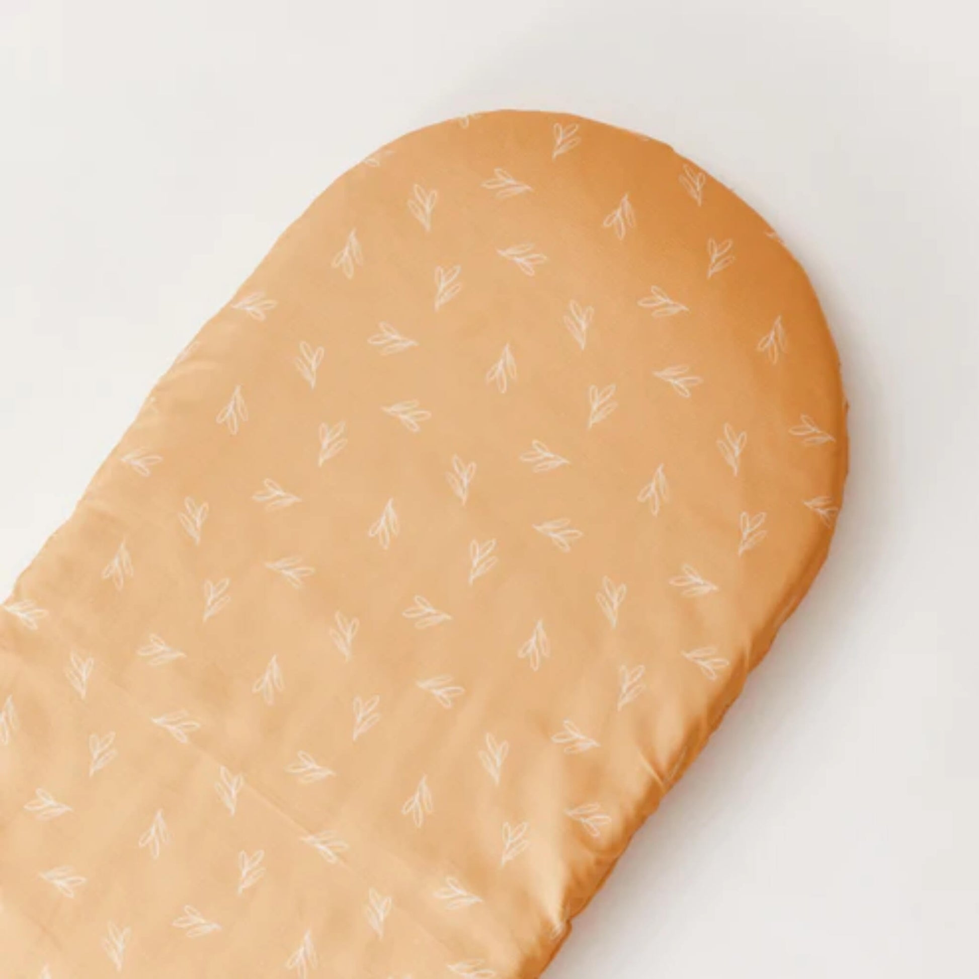 An overhead view of a fitted sheet laid flat, showing an all-over Olive Sprig pattern on warm ochre cotton.