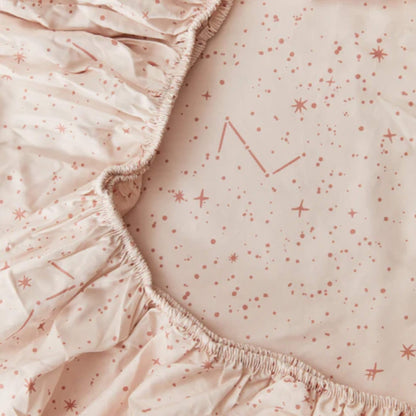 Detail of the elasticated edge on a cream fitted sheet, showing gathered cotton fabric and pink star print underneath.