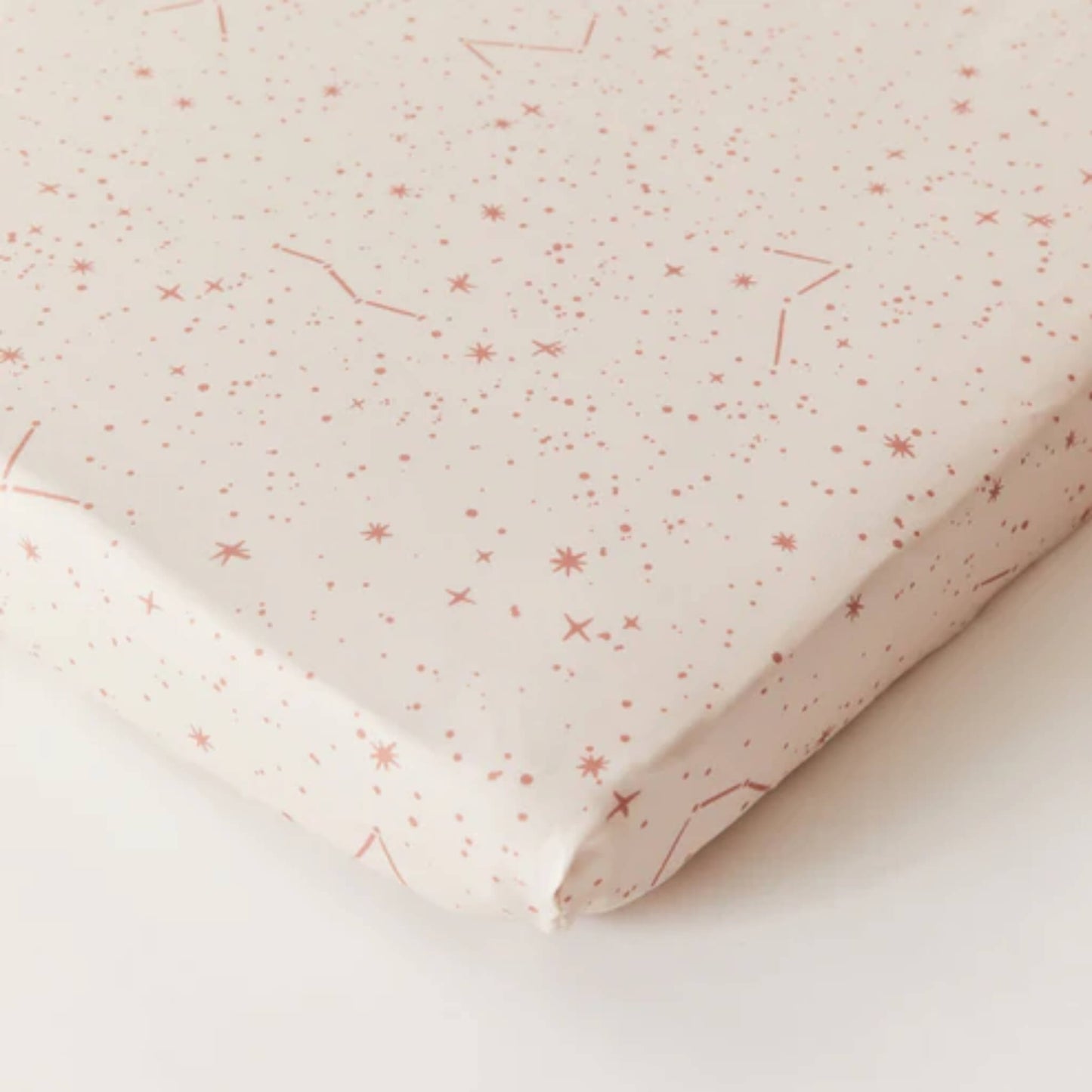 Kabode Starscape fitted cot sheet in cream organic cotton with a soft pink star and constellation print, shown neatly fitted over a mattress corner.