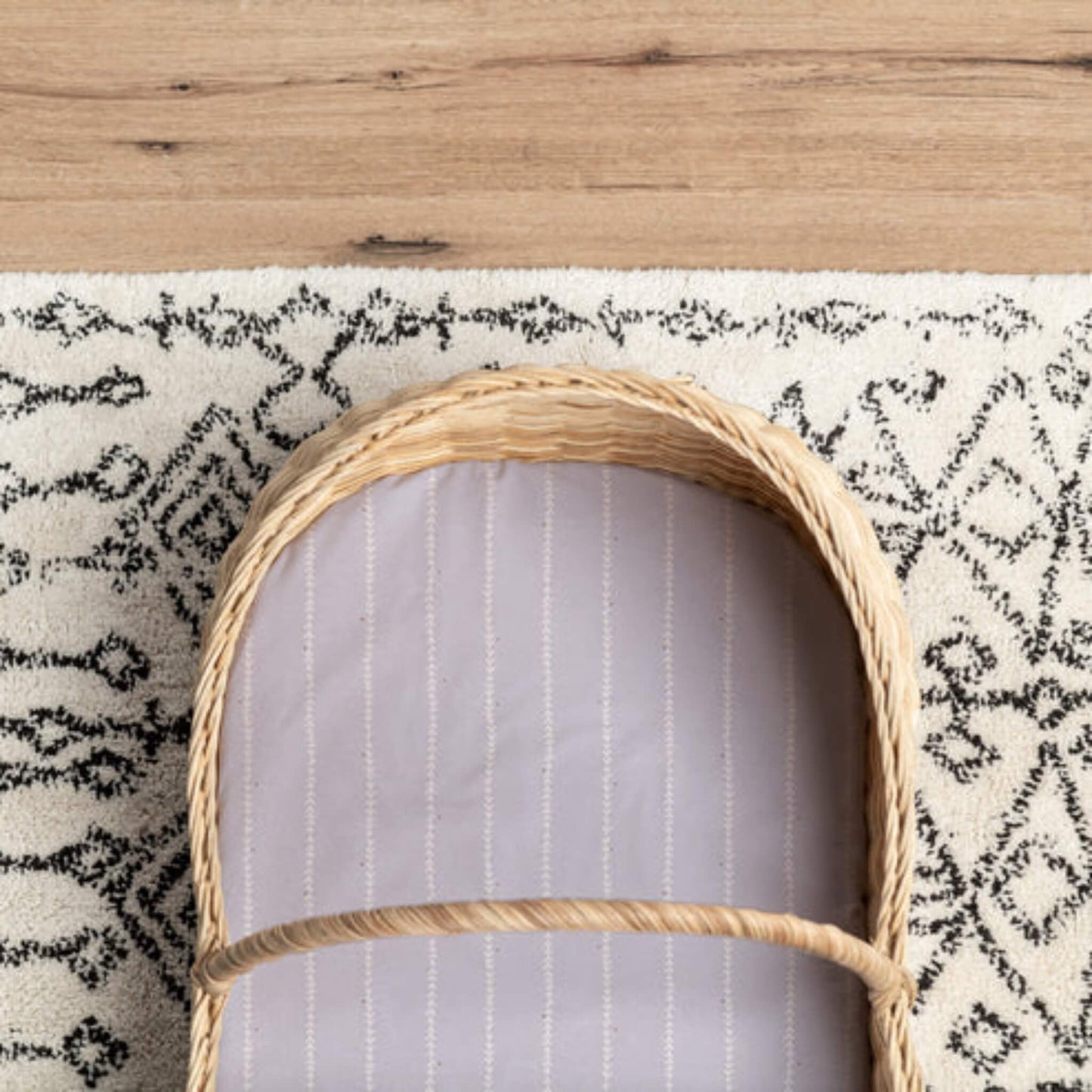 A lilac fitted sheet placed inside a woven Moses basket, showing the fitted shape and striped vine pattern.