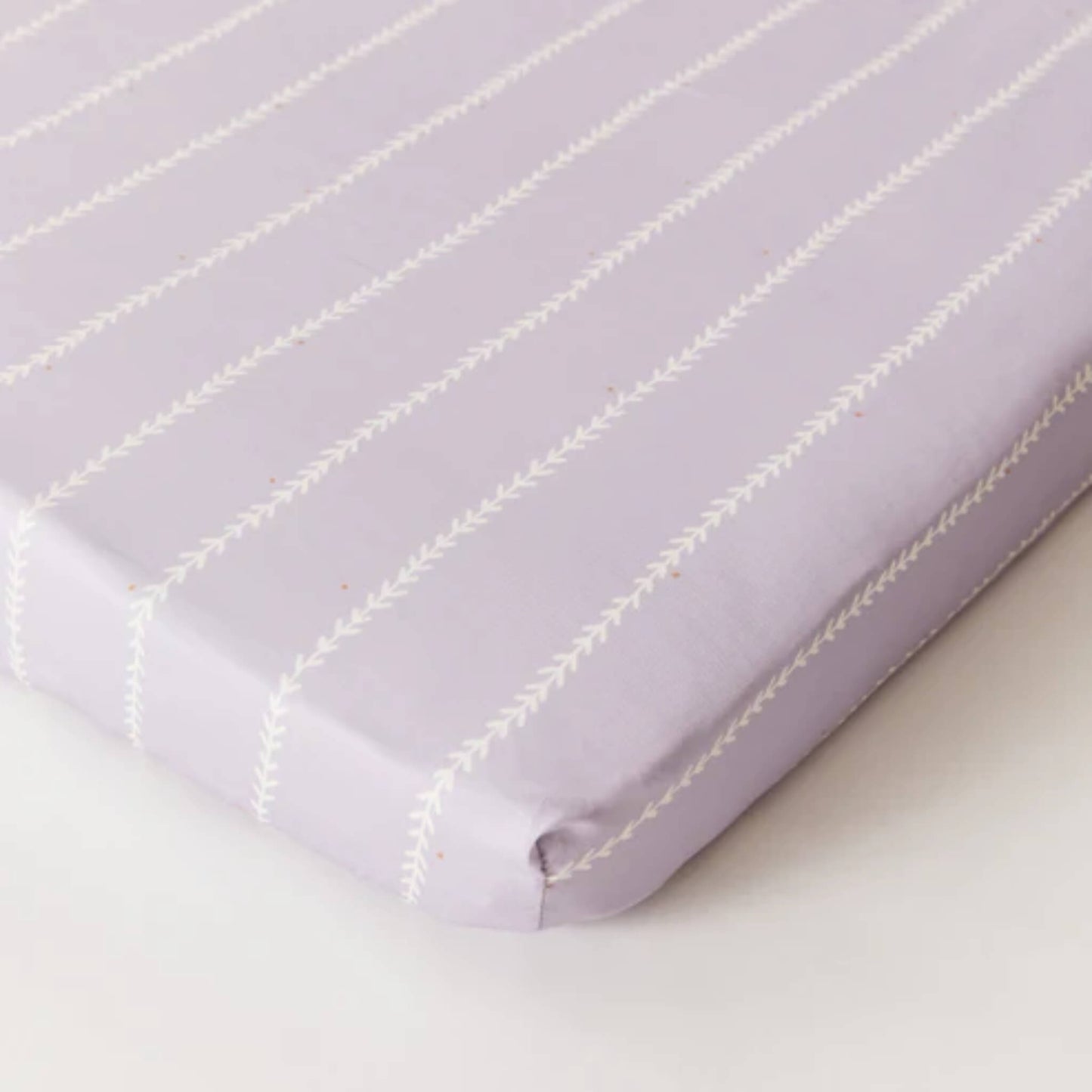 Kabode organic cotton fitted sheet in Vine Lilac, shown fitted on a mattress with a soft lilac base and fine white stitched vine stripes.