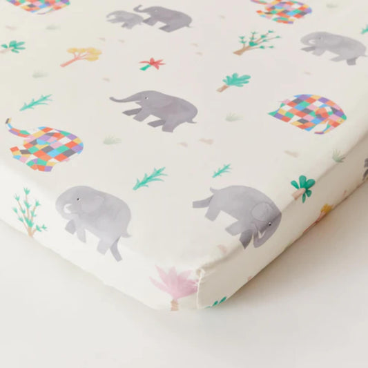 Kabode Organic Cotton Cot Bed Fitted Sheet featuring Elmer the Patchwork Elephant print, shown fitted over a cot bed mattress with playful elephants and trees on soft organic cotton.