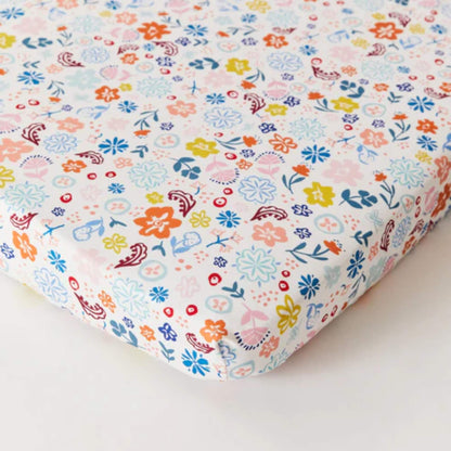 Kabode Organic Cotton Fitted Sheet with a soft cream base and a colourful floral print in blue, pink, yellow, and coral tones, shown neatly fitted over a mattress with elasticated edges.