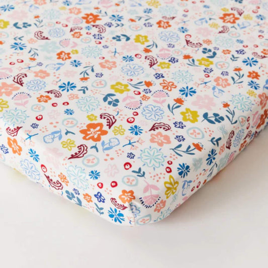 Kabode Organic Cotton Fitted Sheet with a soft cream base and a colourful floral print in blue, pink, yellow, and coral tones, shown neatly fitted over a mattress with elasticated edges.