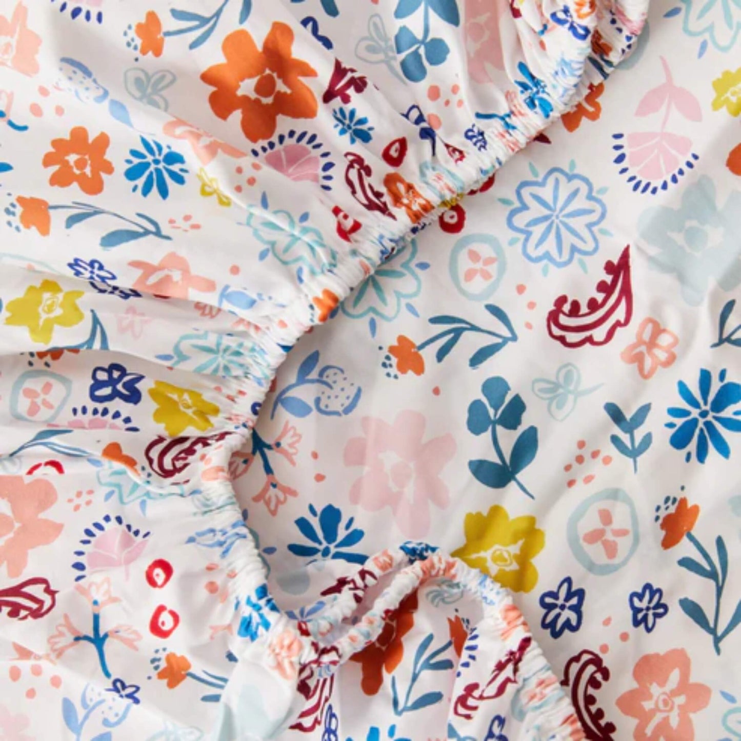 A close-up view of organic cotton fabric gathered at the elasticated edge, showing the smooth weave and detailed floral illustrations.