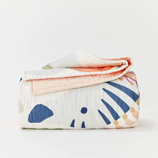 Kabode organic cotton quilt folded neatly to show a floral and animal print outer layer with a soft peach reverse, featuring hand-drawn botanical shapes and gentle stitched quilting.