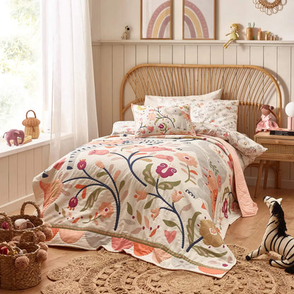 A styled nursery scene with a cot dressed in matching bedding, featuring a floral quilt layered neatly over the mattress and coordinating fitted sheet.
