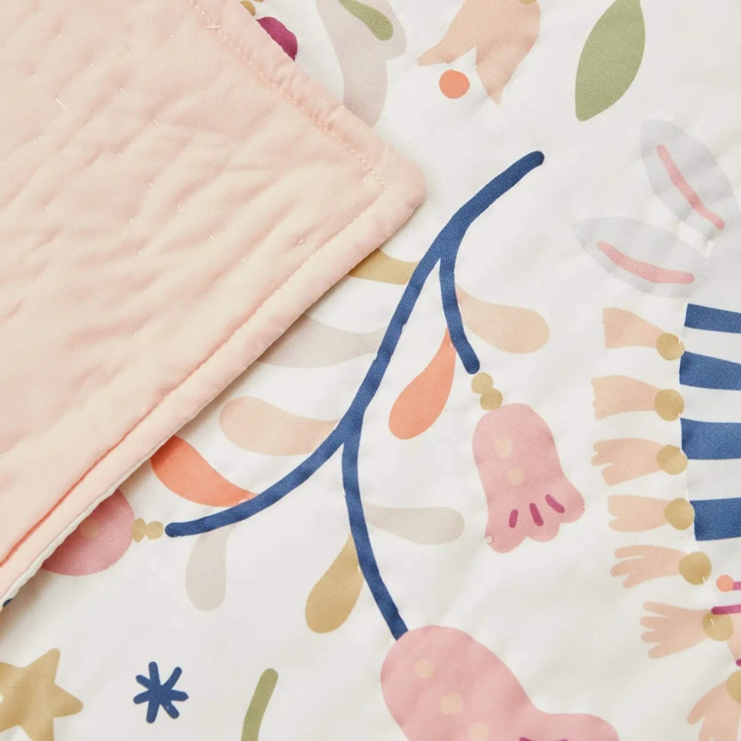 A close-up of quilt fabric showing hand-drawn floral motifs, small animals, and flowing branch details printed on smooth cotton.
