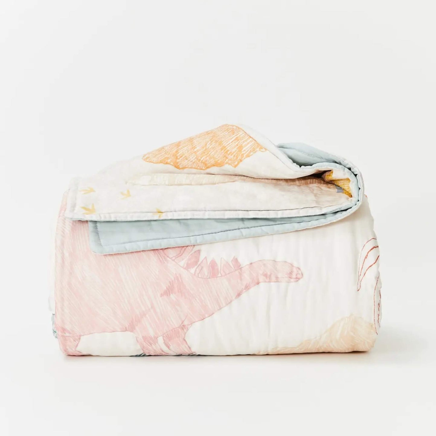 Kabode Organic Cotton Quilt  in Dino design folded neatly to show a hand-drawn dinosaur illustration in soft pastel tones with a pale blue reverse edge.