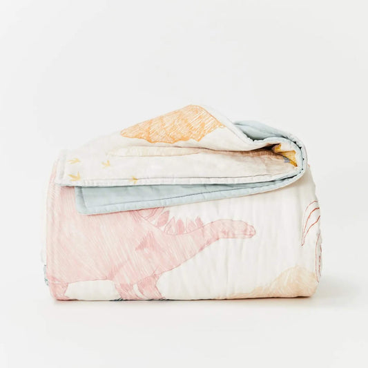 Kabode Organic Cotton Quilt  in Dino design folded neatly to show a hand-drawn dinosaur illustration in soft pastel tones with a pale blue reverse edge.