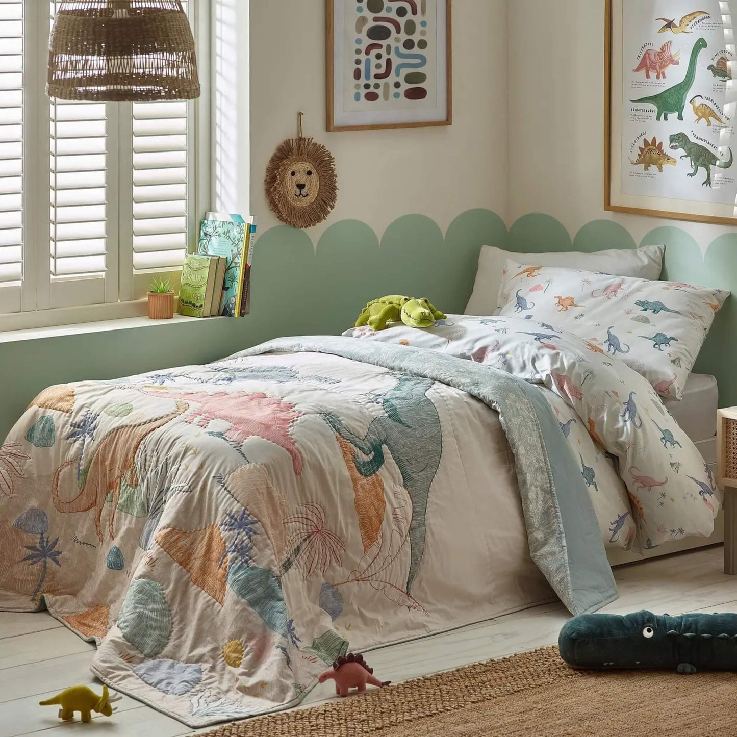 A single child’s bed styled with a dinosaur quilt layered over matching bedding, featuring playful dinosaur illustrations and soft, washed colours.