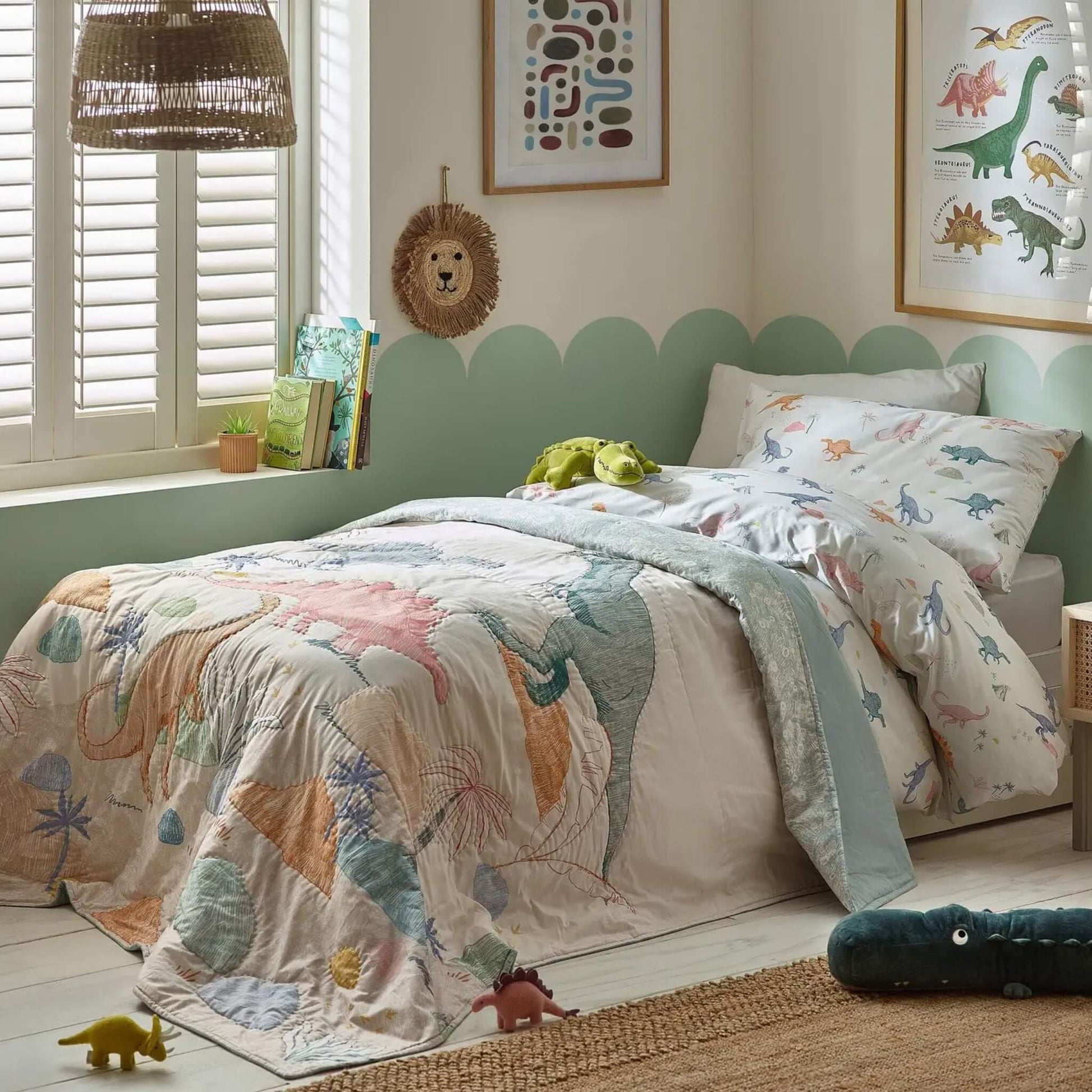 A single child’s bed styled with a dinosaur quilt layered over matching bedding, featuring playful dinosaur illustrations and soft, washed colours.