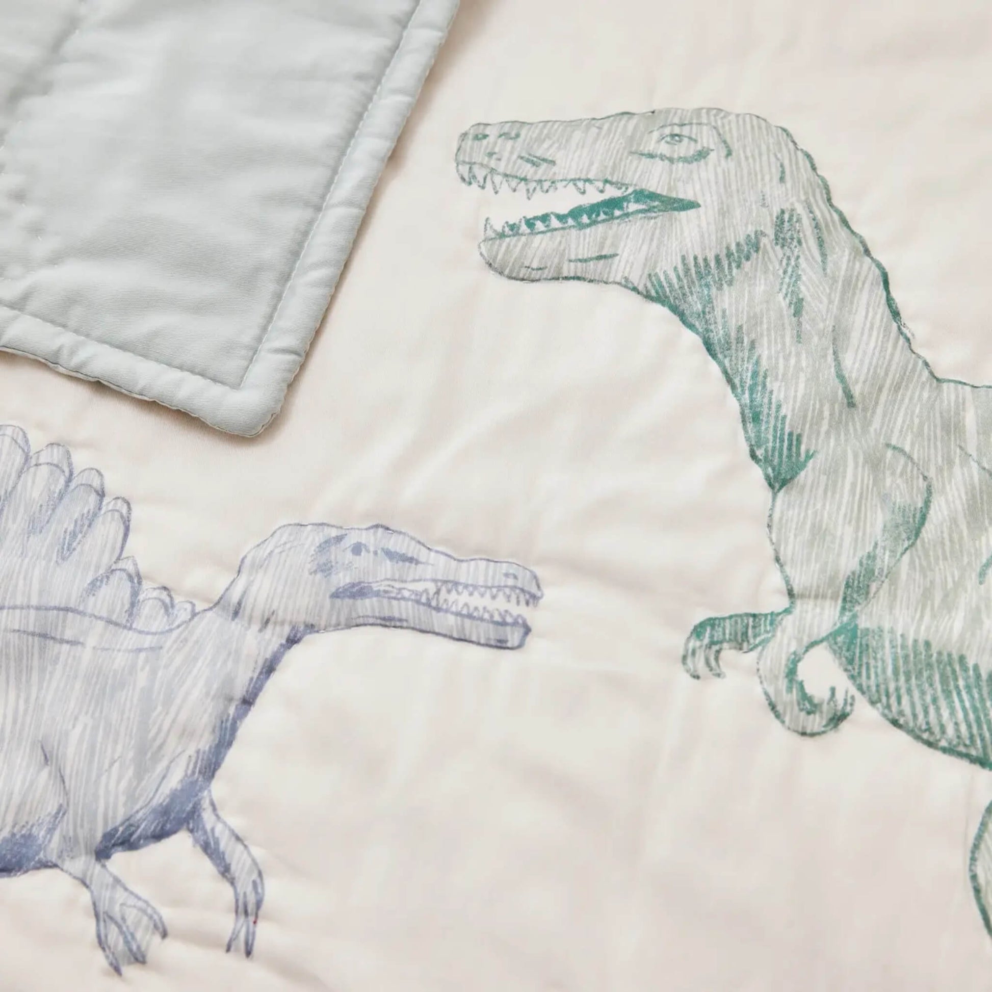 A close-up of a quilted fabric surface showing hand-drawn dinosaur illustrations with visible stitching and a smooth cotton finish.