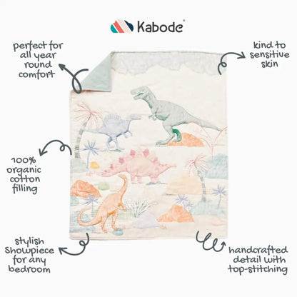 A full view of a dinosaur-patterned quilt laid flat, highlighting illustrated dinosaurs, palm trees, and soft landscape details with top-stitched edging.