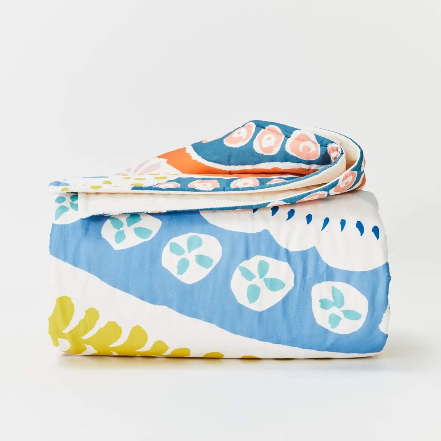 Kabode Organic Cotton Quilt – floral design folded neatly to show layered stitched cotton with curved floral motifs in blue, coral, mustard, and soft green tones.