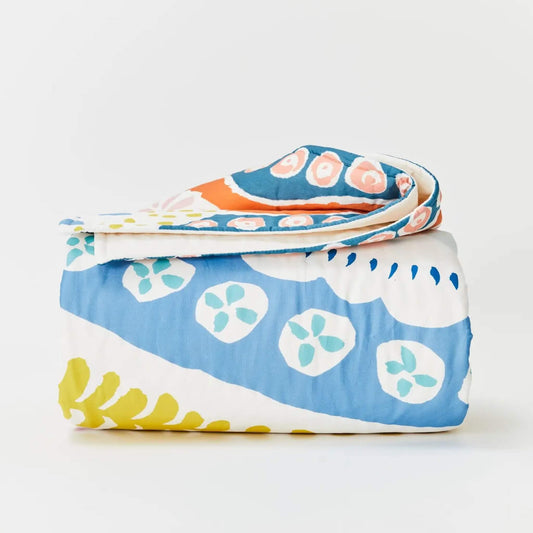 Kabode Organic Cotton Quilt – floral design folded neatly to show layered stitched cotton with curved floral motifs in blue, coral, mustard, and soft green tones.