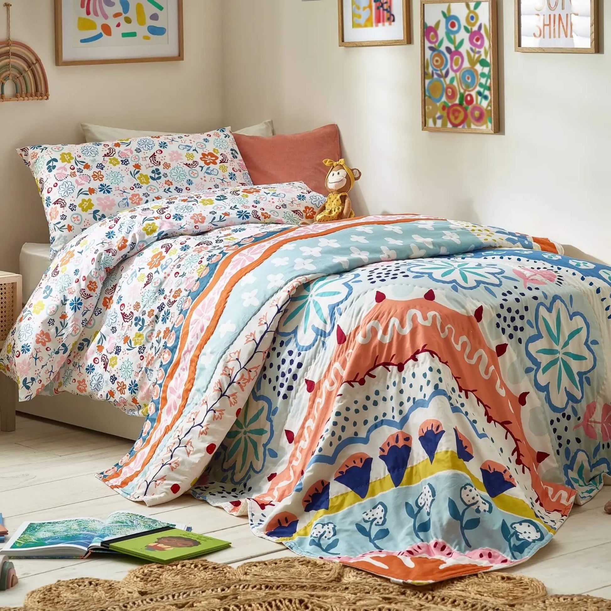 A child’s single bed styled with a floral quilt layered over matching bedding, featuring bold curved patterns, scattered floral shapes, and soft contrasting colours.