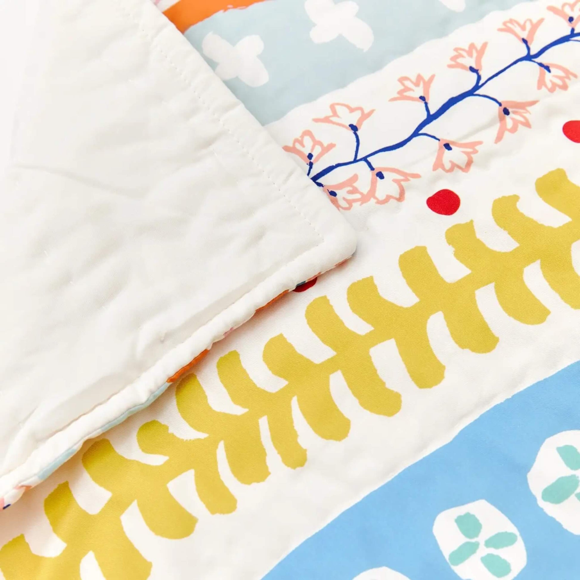 A close-up of quilted cotton fabric showing stitched edges, a pale backing, and printed floral bands in mustard yellow and soft blue.