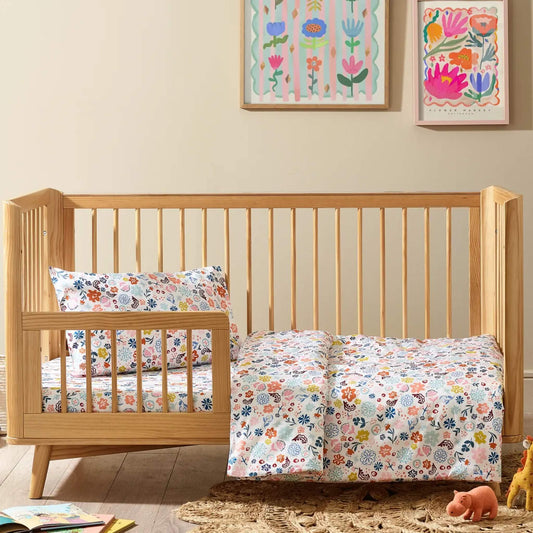 Kabode cot bed duvet cover and pillowcase set in a colourful floral print, styled on a wooden cot bed with matching bedding in soft organic cotton.