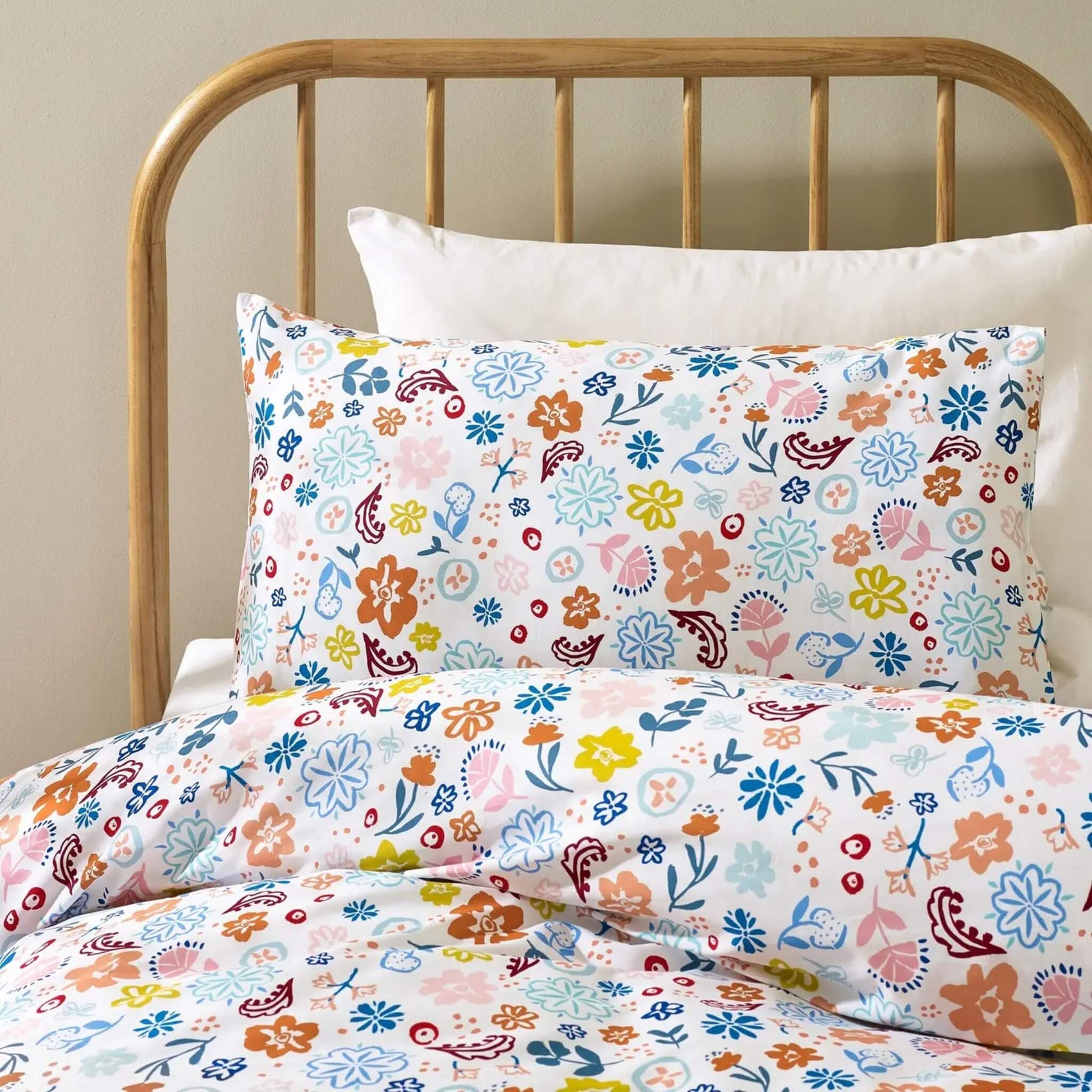 Close-up view of  a pillowcase showing a dense floral print with stylised flowers, leaves, and decorative shapes printed on smooth organic cotton.