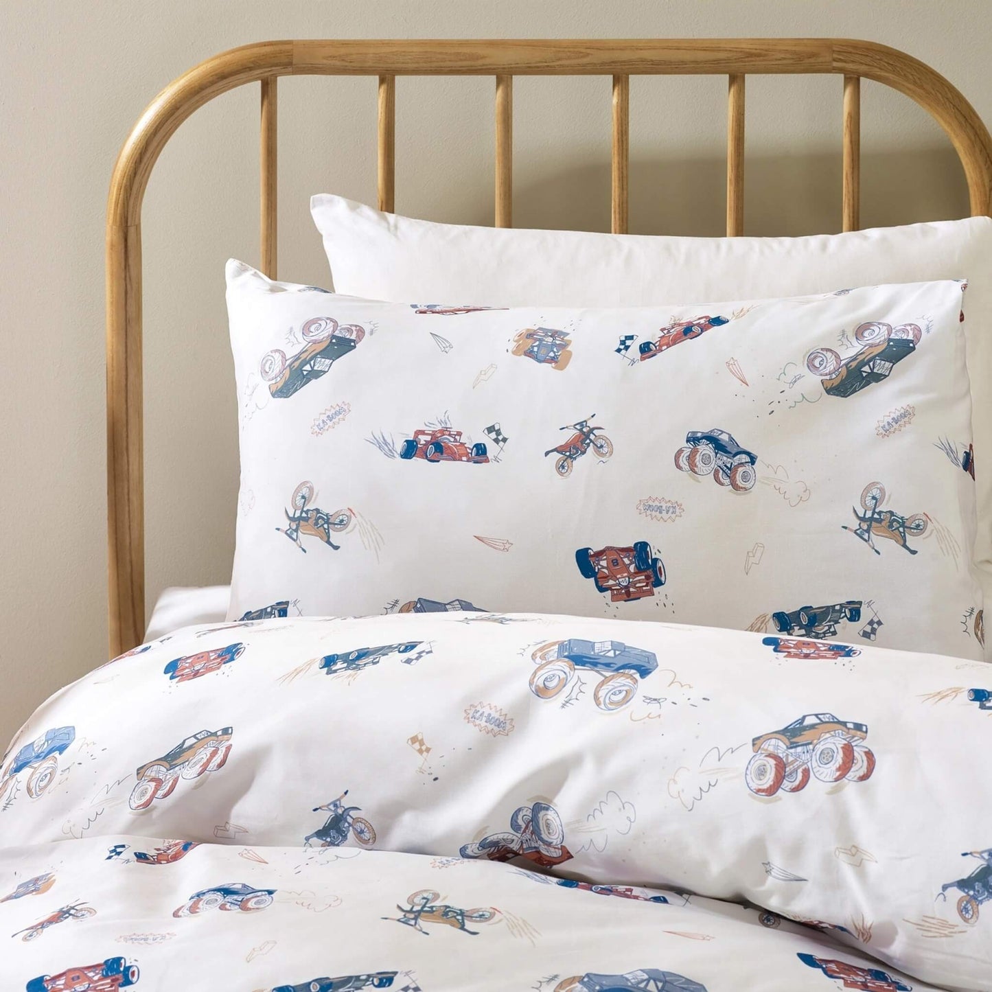 Close view of a pillow resting against white bedding, showing repeating vehicle illustrations with fine line details and muted blue, red, and neutral tones.