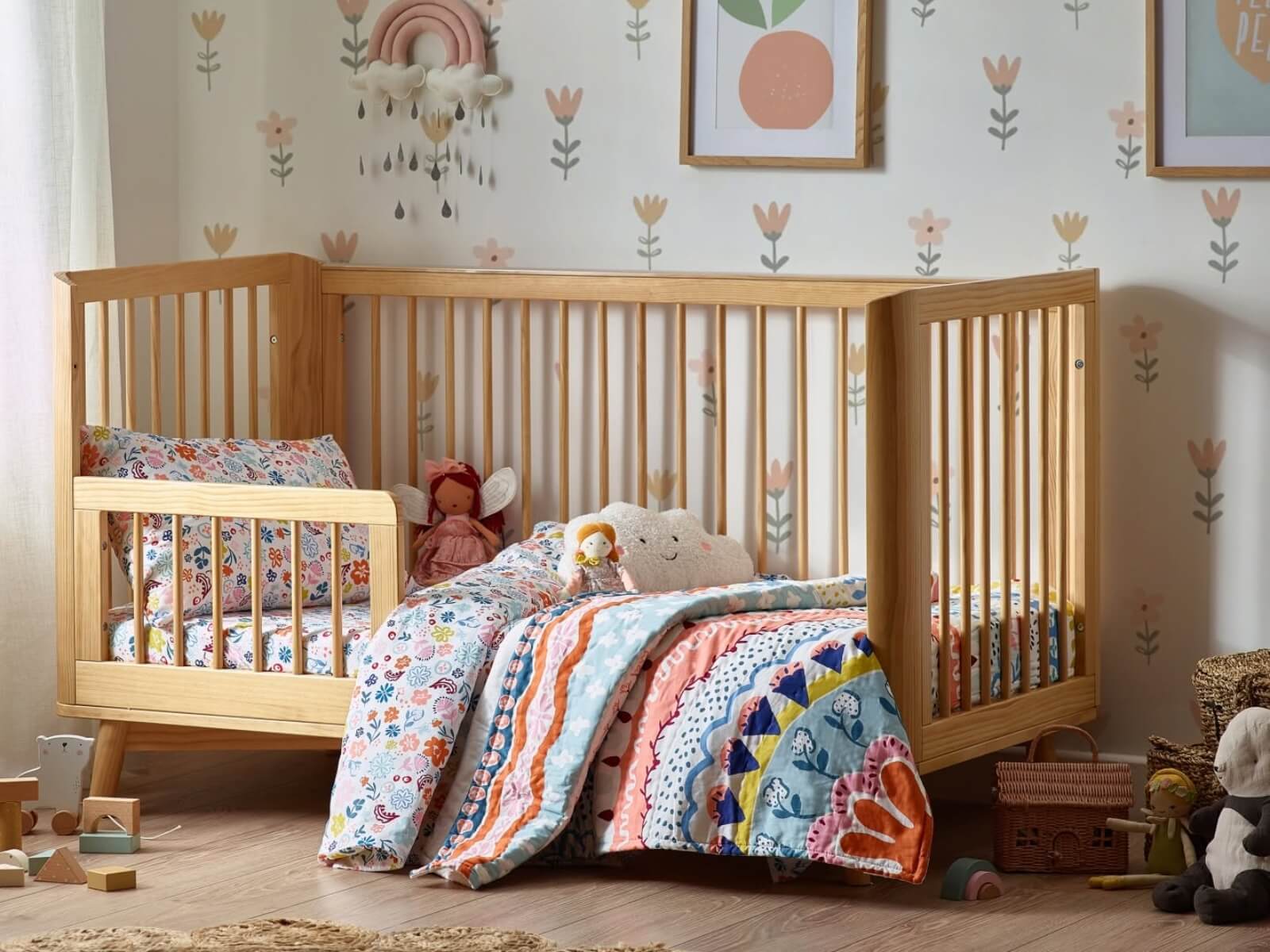 Wooden cot bed converted into a toddler bed in a modern nursery with colourful bedding and soft toys.