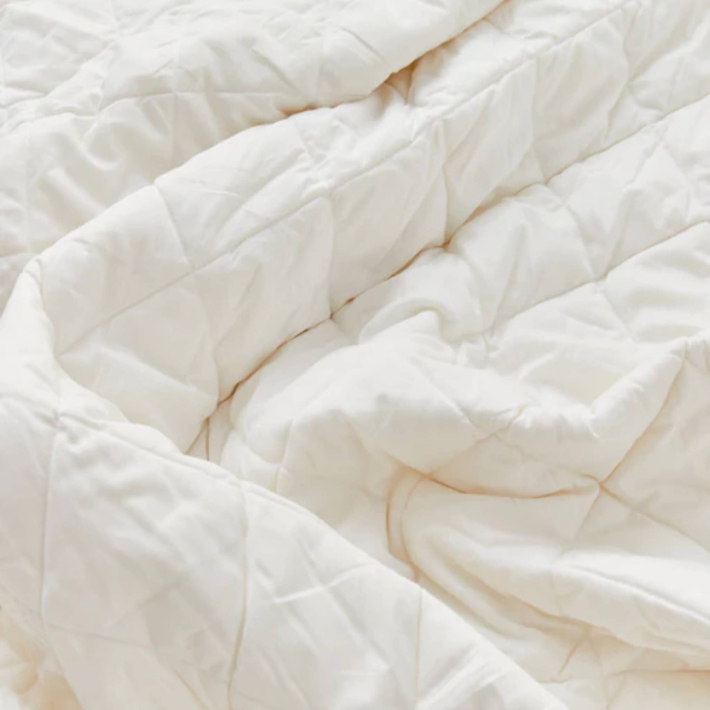 Close-up of quilted cream duvet fabric with stitched square pattern, showing soft padding and breathable cotton texture.