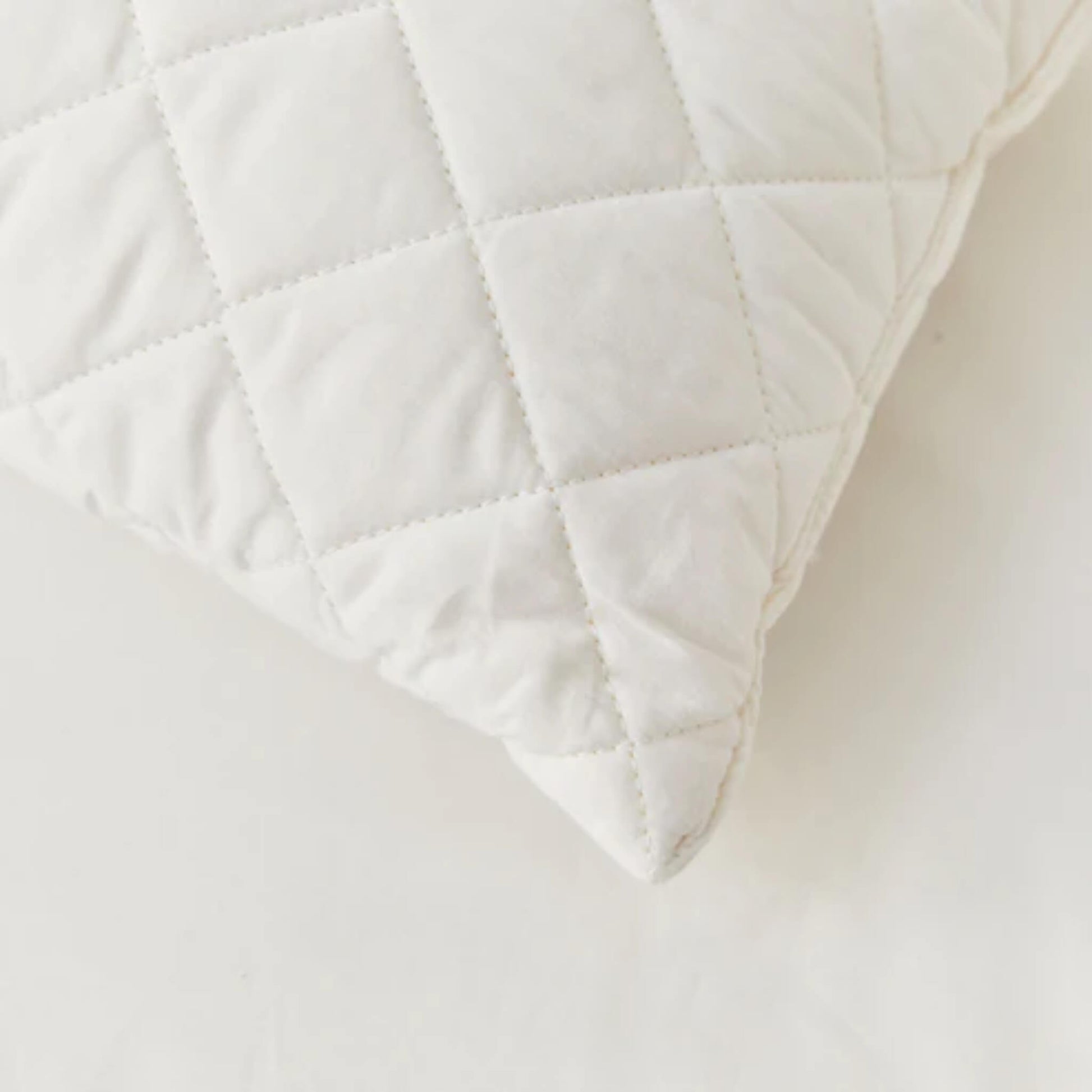 Close-up of a quilted pillow corner showing diamond stitching, soft cotton fabric and gentle padding detail.