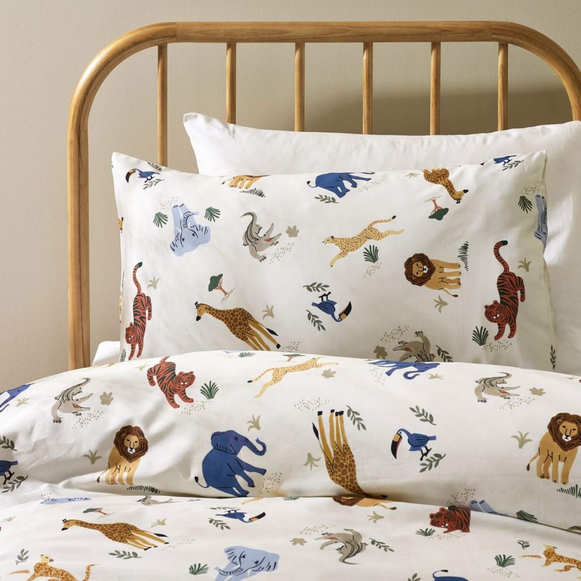 Close-up view of a cream duvet cover and pillowcase showing illustrated safari animals including elephants, lions, giraffes and birds printed on smooth cotton bedding.