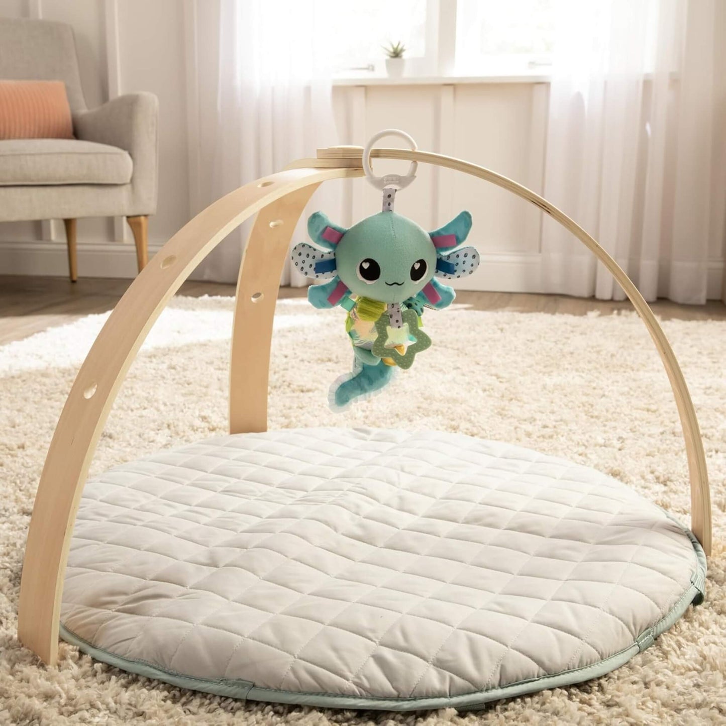 Plush axolotl toy clipped to a natural wood baby play gym arch above a quilted mat in a softly lit nursery.