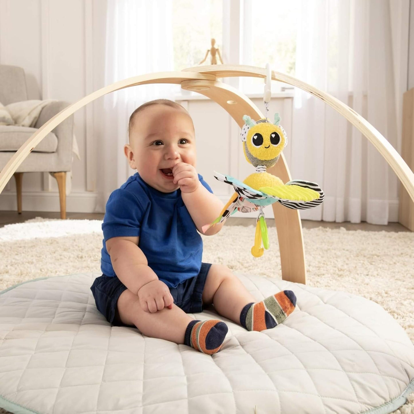 Smiling baby sitting on a play mat reaching for the hanging bee toy.