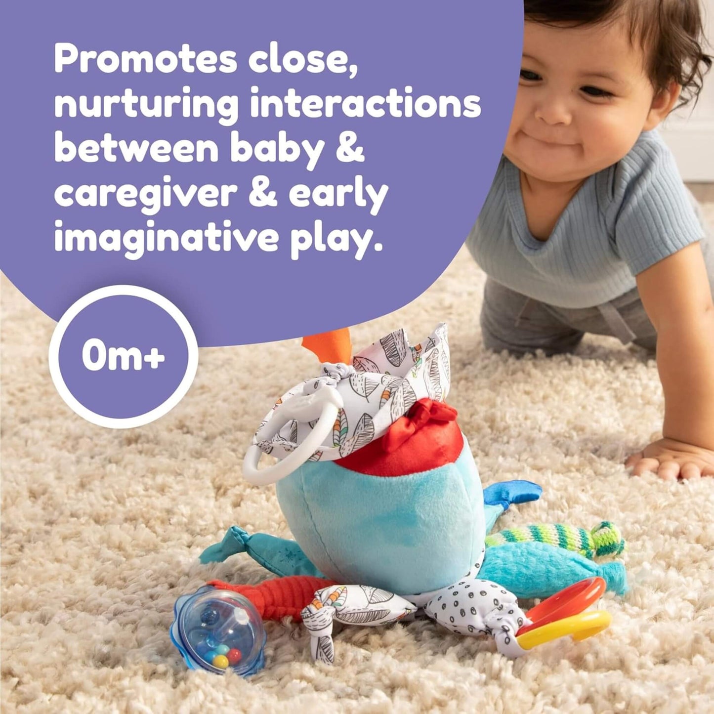 A baby crawling on a soft rug toward a colourful fabric activity toy lying on the floor with textured legs and bright features.