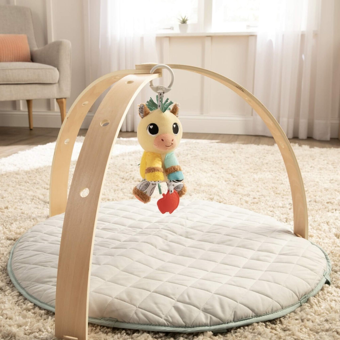 Plush horse baby toy clipped to wooden play gym, positioned over quilted mat in a bright room.