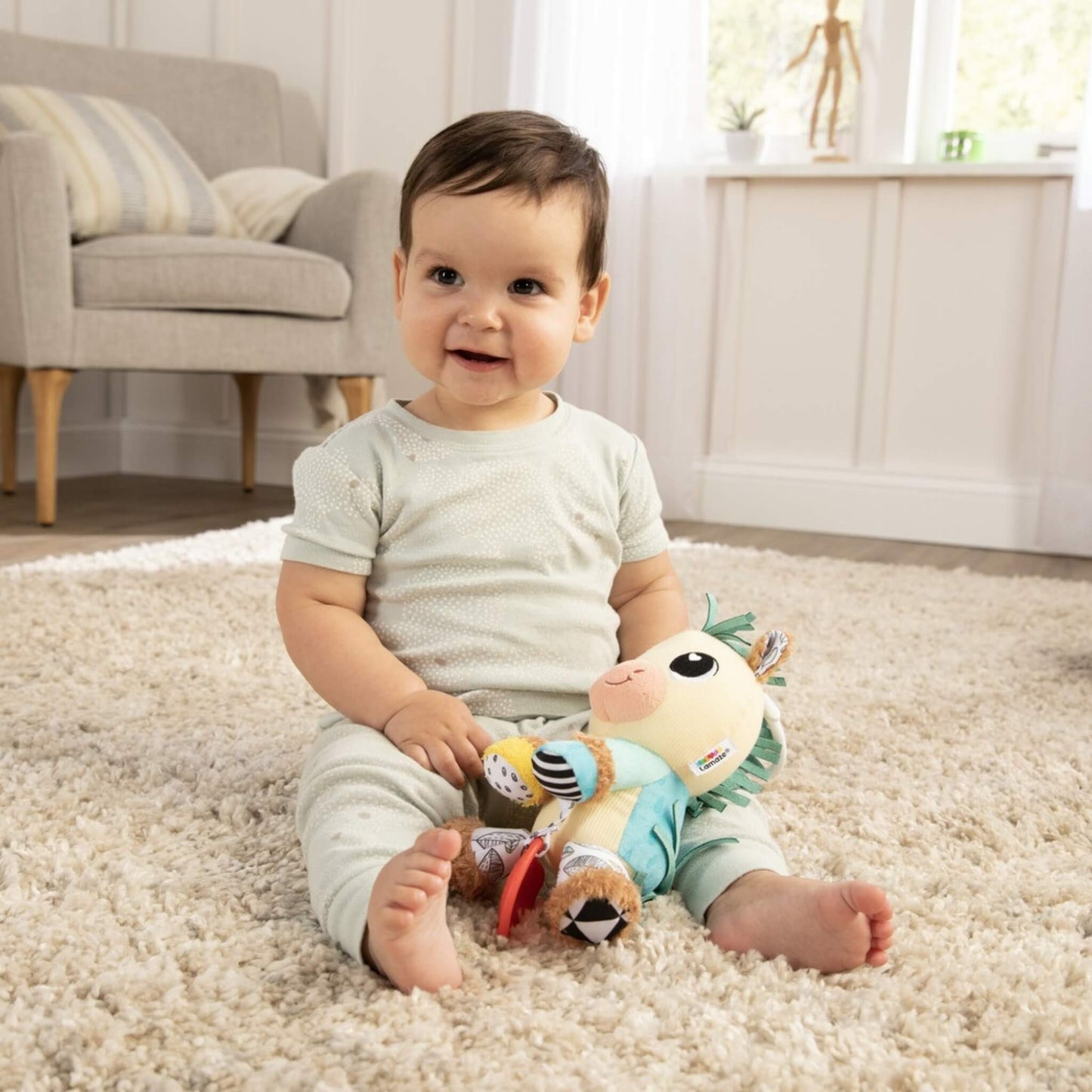 Baby sitting on soft rug holding plush horse toy with bright patterned legs and soft textures.