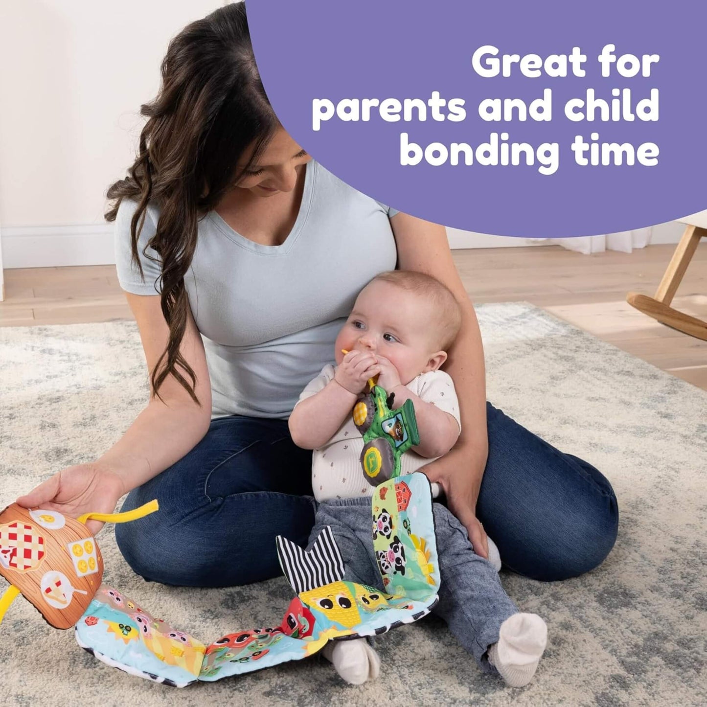 Mother holding a baby who is mouthing a soft tractor teether attached to a fabric farm-themed sensory book.