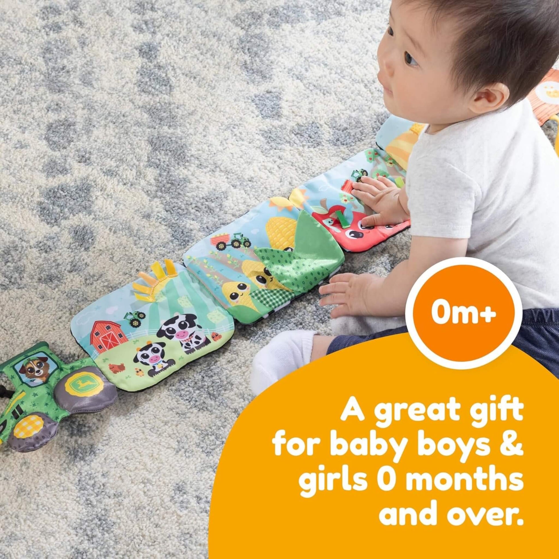 Baby sitting on the floor, touching the textured pages of a fold-out farm-themed activity book filled with bright colours and animal designs.